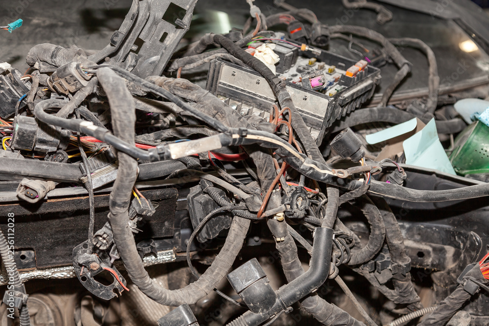 A large tangle of ravel multicolored wires from the car wiring lies in the cabin of the dismantled car with connectors and plugs, a view through the window inside the battered car.