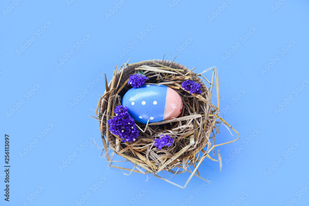 Obraz premium Easter eggs in basket nest decoration with purple statice flowers on blue background