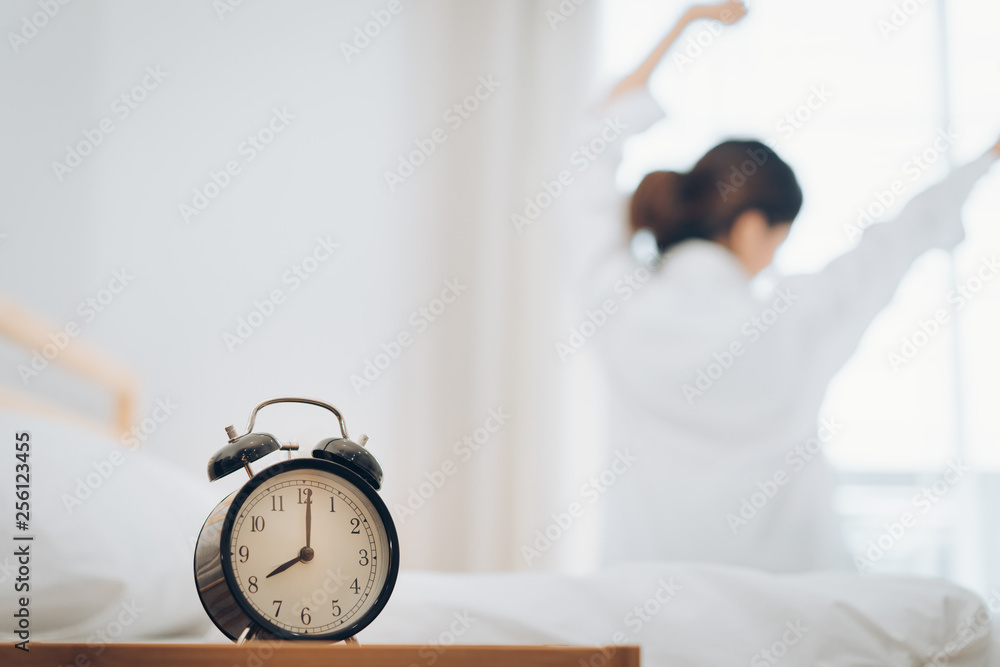 Woman wake up with alarm clock at moring her stretch on bed at home. - obrazy, fototapety, plakaty 
