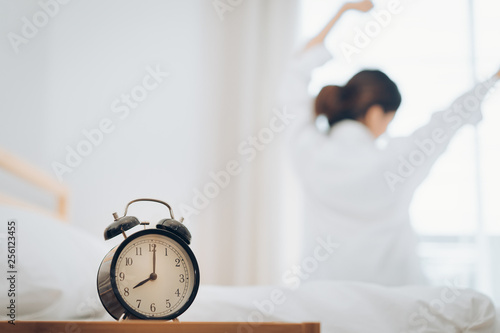 Woman wake up with alarm clock at moring her stretch on bed at home.