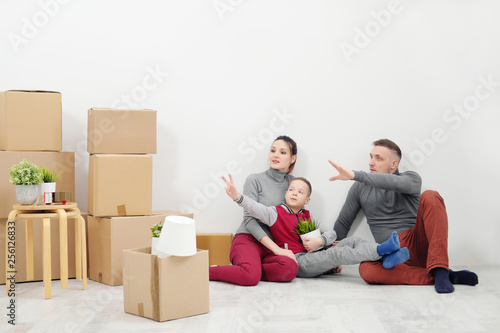 Young family, man woman and child son sits at floor in new apartments. Boxes with cargo on a white background.