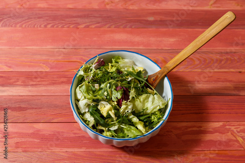 Fresh vegetarian salad from escariol, frieze, radicio, arugula in a white plate on a wooden background. photo