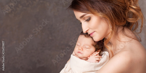 Pretty young woman holding a newborn baby in her arms. Portrait of mother and little baby. Happy family concept.