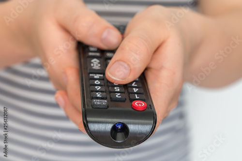 Remote control in female hands pointing to TV