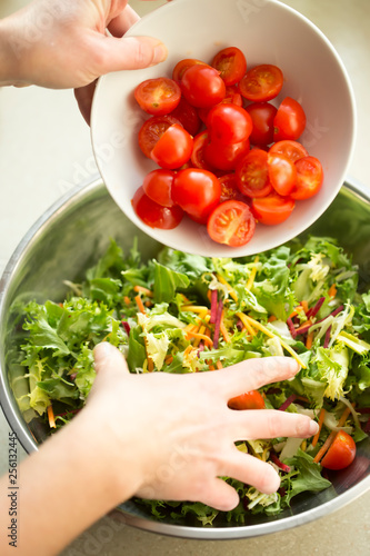 Hands mixing mixed leaves with tomatoes salad preparation