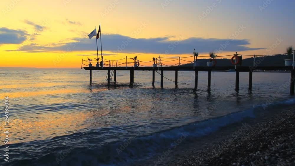 Silhouette of a pier with flag at sunrise on the sea in Kemer, Turkey Silhouette of a pier with flag at sunrise on the sea in Kemer, Turkey