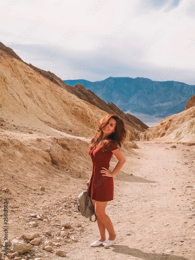 Girl with long hair in a red dress walking on a sandy canyon in the Valley of Death