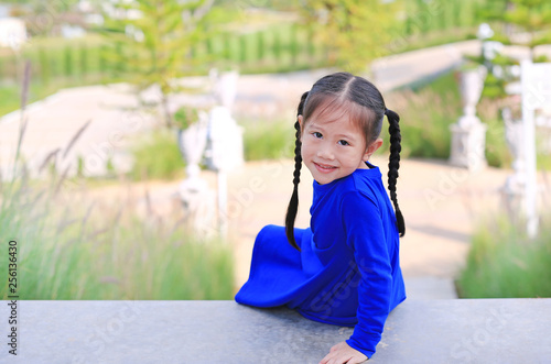 Adorable little Asian child girl sitting on stair in the garden with looking camera.