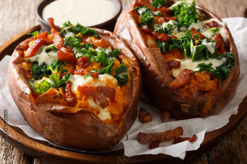 Delicious whole baked sweet potato with fresh kale, bacon and cheese sauce close-up on a plate. horizontal