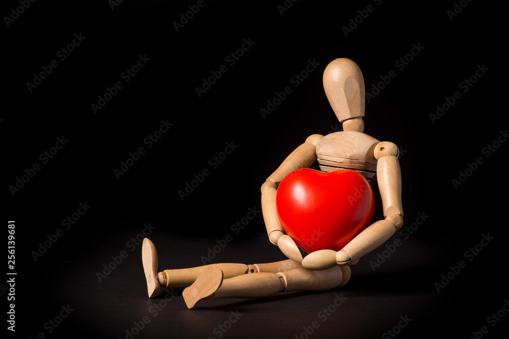 Wooden puppet with a red heart in his hands on a black background