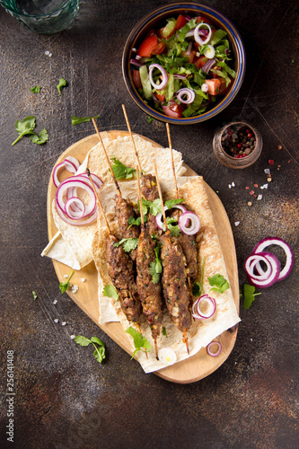 Lula kebab from minced meat (beef, lamb, veal) on pita bread (lavash), shish kebab. With red onion, cilantro and vegetable salad