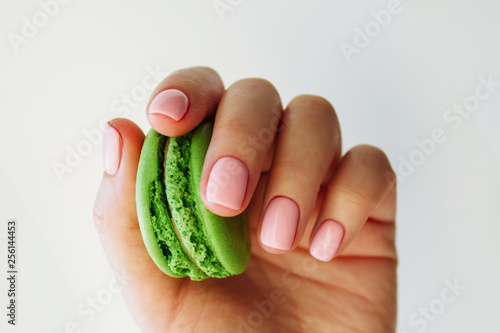 Hand with light rose manicure with bright green macaron. Isolated at white background.