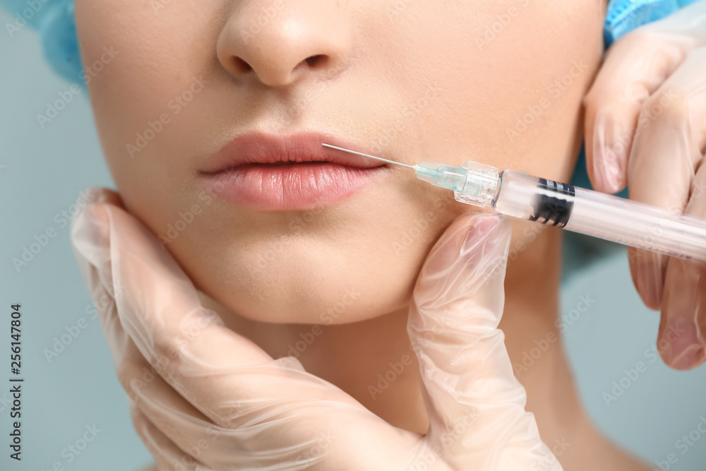 Young woman receiving injection in face on color background, closeup