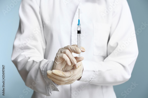 Cosmetologist holding syringe with filler on color background, closeup