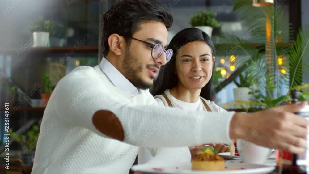 Romantic couple having date in cafe: middle eastern man pouring tea for young asian girlfriend, they smiling and talking Romantic couple having date in cafe: middle eastern man pouring tea for young asian girlfriend, they smiling and talking
