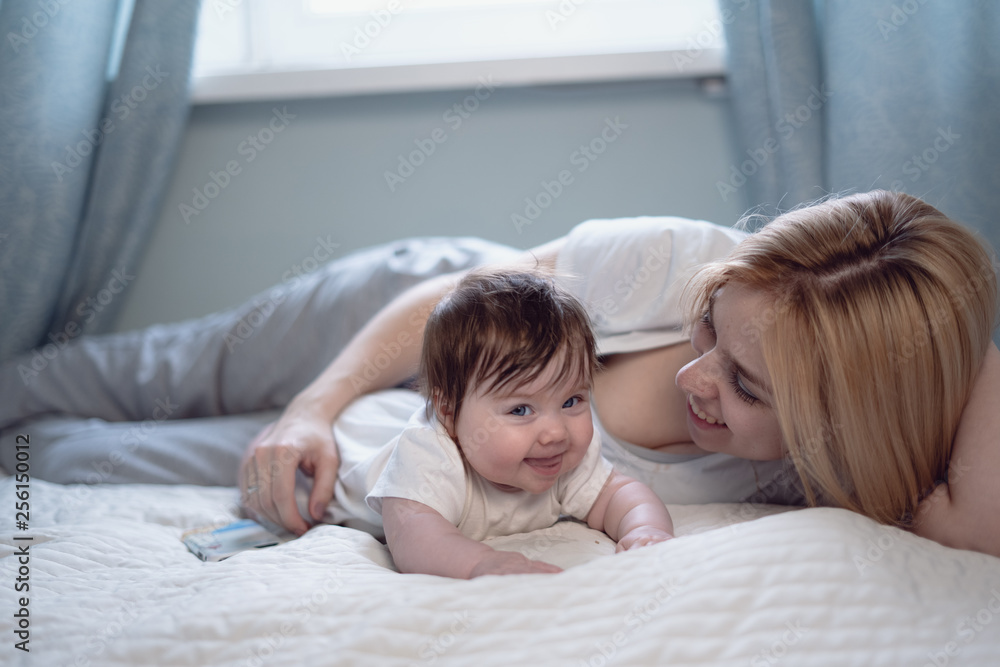 Happy smiling mother and baby lying on bed at home Happy smiling mother and baby lying on bed at home