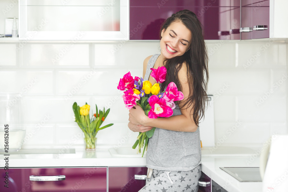 Young attractive woman holding flowers. Lady on the kitchen with tulips. Housewife in the morning standing on the home kitchen. Young attractive woman holding flowers. Lady on the kitchen with tulips. Housewife in the morning standing on the home kitchen.
