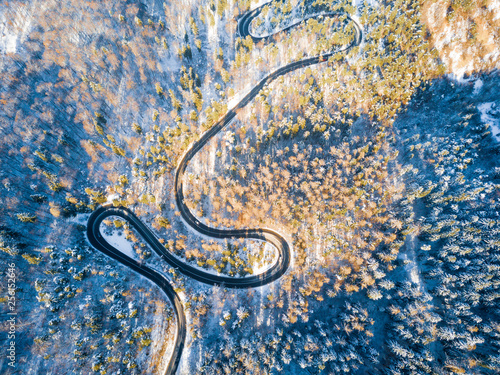 Beautiful aerial view of snow covered mountain landscape in winter time with curvy road cutting through forest. Aerial view by drone . Romania 