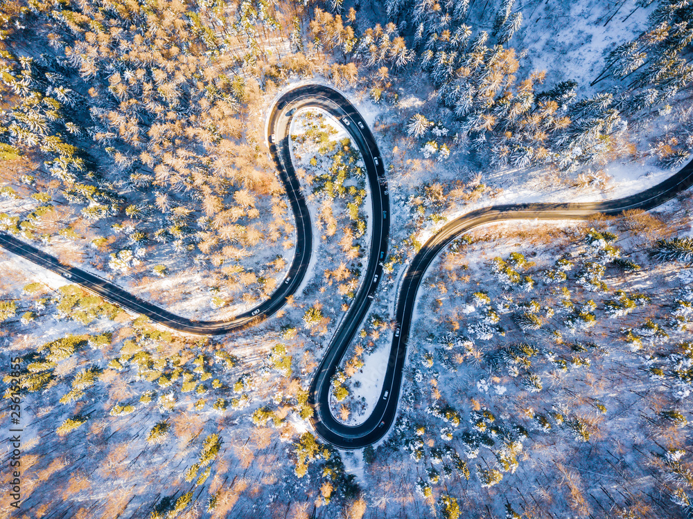 Beautiful aerial view of snow covered mountain landscape in winter time with curvy road cutting through forest. Aerial view by drone . Romania	
