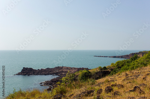 hillside with dry and green grass against a blue ocean with a rocky shore in the sea © Pavel