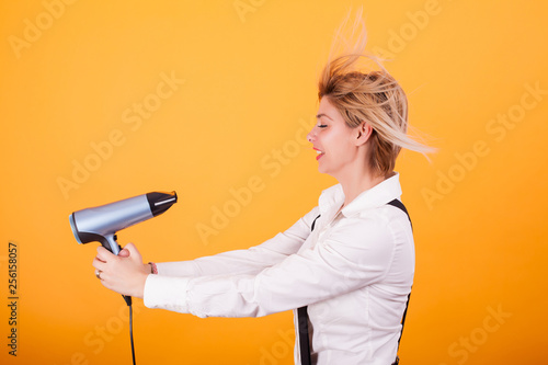 Принти на полотні Young funny woman blowing her short hair with a hair drayer over yellow background