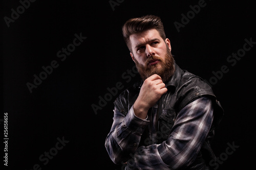 Dramatic portrait of beard man wearing a leather vest over black background © DC Studio