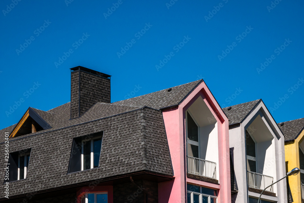 Rows of triangular elements of roofline covered with shingle, with chimney against blue sky