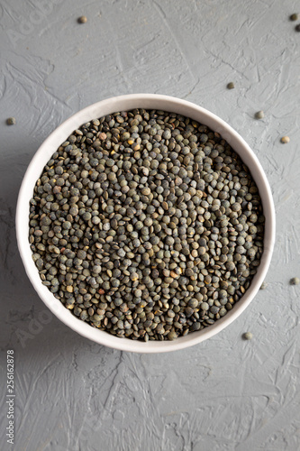 Dry green french lentils in a gray bowl over concrete background, overhead view. Top view, from above, flat lay.