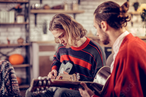 Young man wearing striped sweater learning to play guitar