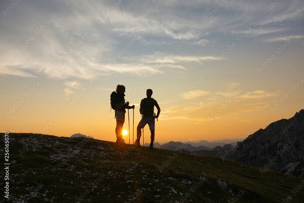 SILHOUETTE Young male and female hikers rest and observe the sunset after ascent SILHOUETTE Young male and female hikers rest and observe the sunset after ascent