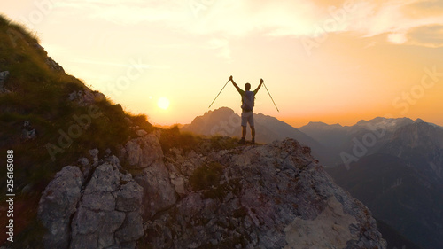 LENS FLARE: Excited man outstretches arms as he sees the sunset from a cliff.