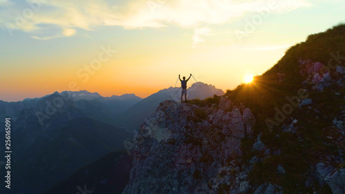 DRONE  Golden morning sun rays shine on excited trekker standing on a cliff.