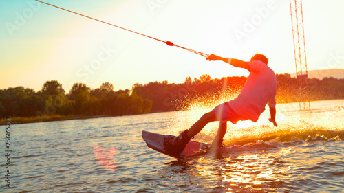 Photos SUN FLARE: Unrecognizable athletic man wakesurfing on the lake at golden sunset