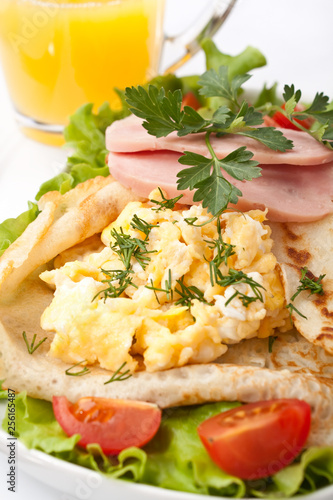 Brunch pancakes with scrambled eggs, ham and tomatoes
