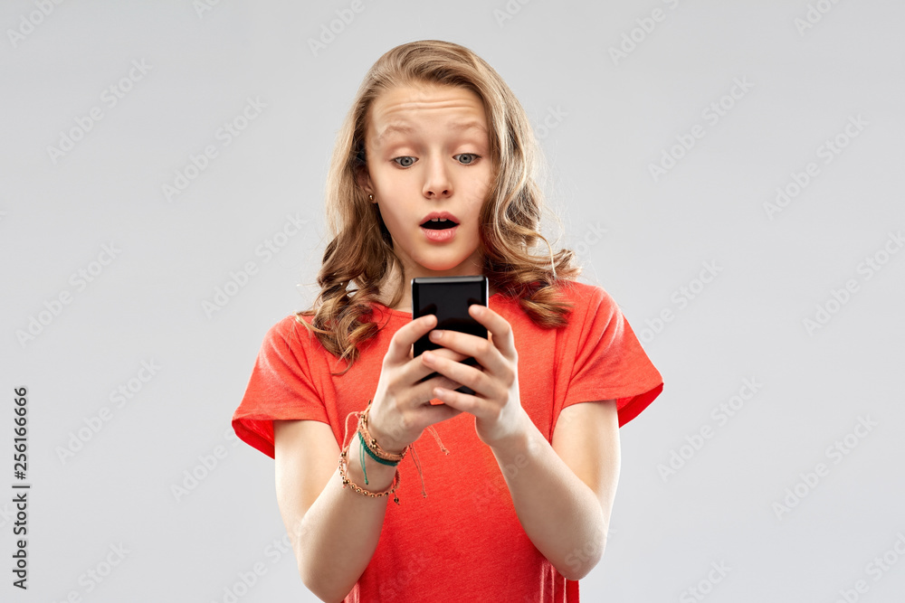 technology, emotions and people concept - terrified teenage girl in red t-shirt using smartphone over grey background technology, emotions and people concept - terrified teenage girl in red t-shirt using smartphone over grey background