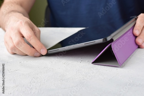 Blurred caucasian man using a digital tablet. White man puts on a new purple leather case on tablet with selective focus. male hands are holding a new tablet and putting on a violet cover. 