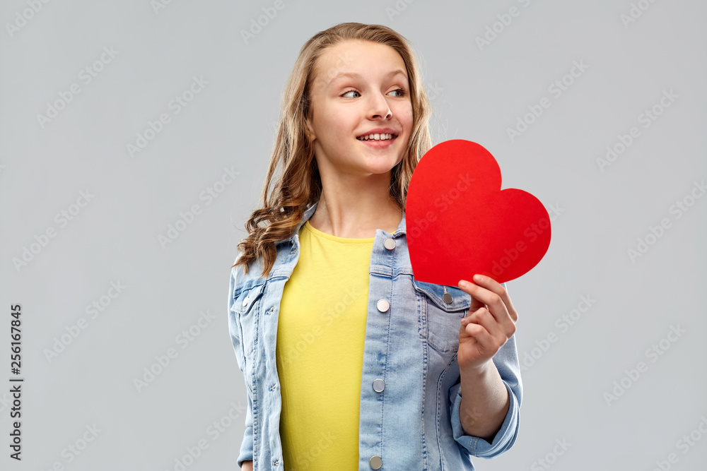 valentine's day, love and people concept - smiling pretty teenage girl in denim jacket holding red heart over grey background valentine's day, love and people concept - smiling pretty teenage girl in denim jacket holding red heart over grey background