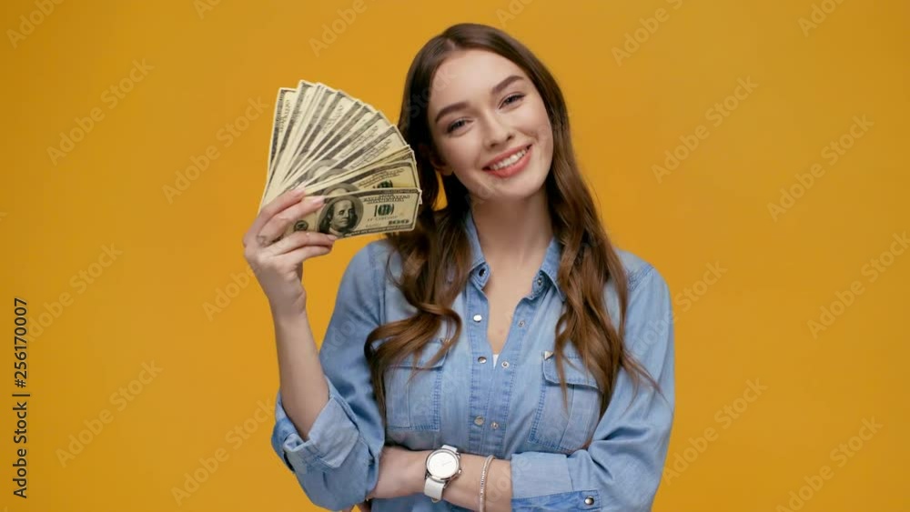 beautiful girl looking at camera, waving dollar banknotes and smiling isolated on yellow beautiful girl looking at camera, waving dollar banknotes and smiling isolated on yellow