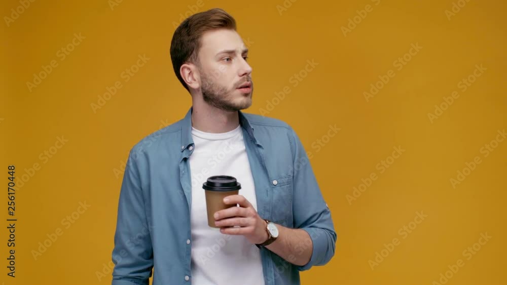 handsome man drinking coffee to go, looking at camera, smiling and showing paper cup at camera isolated on yellow handsome man drinking coffee to go, looking at camera, smiling and showing paper cup at camera isolated on yellow