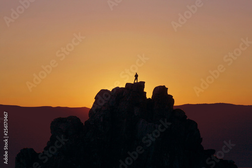 silhouette of a man standing on top of a mountain against the sunset sky