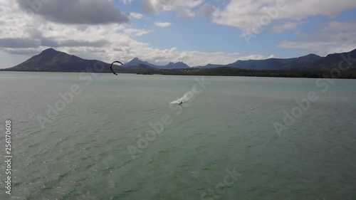sea extreme summertime,kite boarding,man with black kite surfing and having extreme activities in the horizon of the sea.perfect vacation.mountain hills,blue sky,big clouds in mauritius.drone 4K 30fps