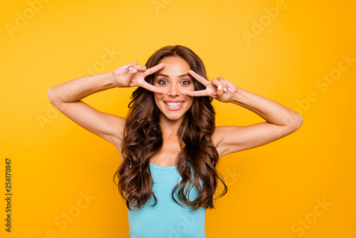 Close up photo amazing beautiful her she lady dreamer excitement show v-sign near eyes both hands arms white toothy wearing blue teal green everyday short dress clothes isolated yellow background