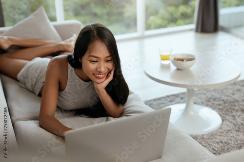 Woman with laptop computer on sofa in living room at home