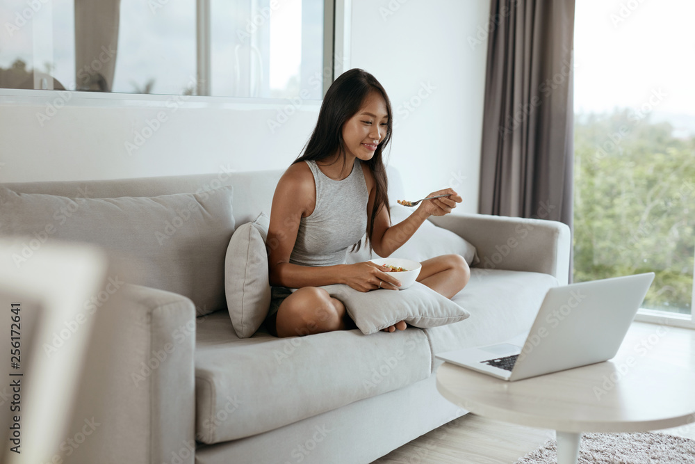 Woman having breakfast while using computer at home in morning Woman having breakfast while using computer at home in morning