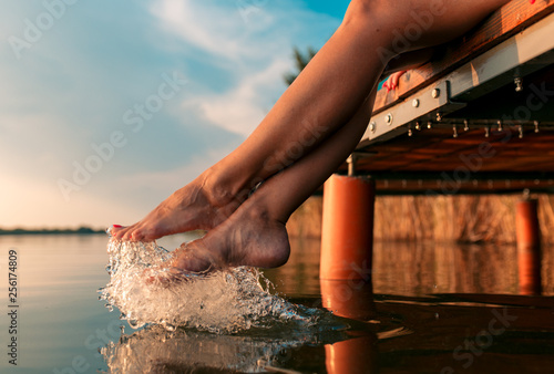 Fototapeta Woman legs as she sitting on wooden dock by the lake.