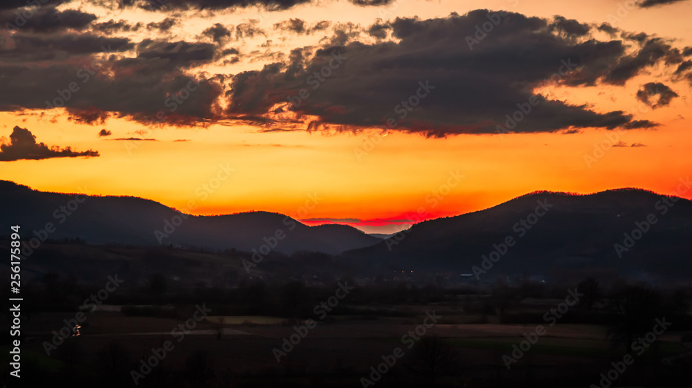 Beautiful colorful sunset with orange cloud sky. Rural landscape with hills and mountains.