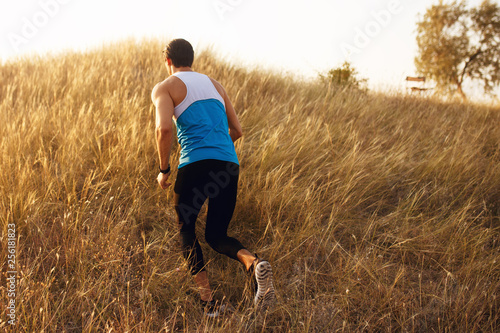 Image of a strong, athlete, muscular, fit, sexy runner man stands back in sportswear outside, isolated on a beautiful sunset landscape background. Copy space. © Dragosh