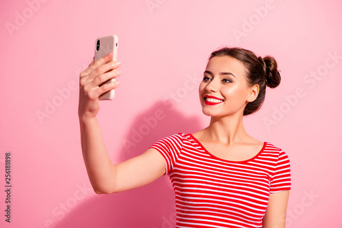 Close-up portrait of nice cute charming attractive lovely magnificent winsome cheerful girl wearing striped t-shirt holding in hand gadget taking making selfie isolated on pink pastel background photo