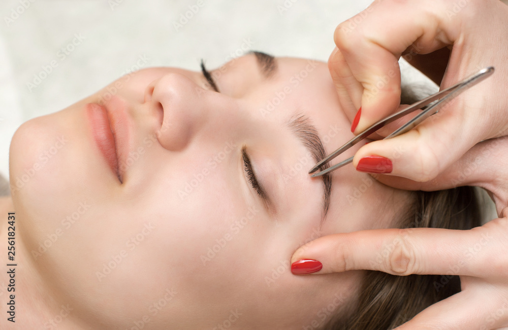 The make-up artist plucks her eyebrows from a young woman in a beauty salon. Professional skin care and make-up.