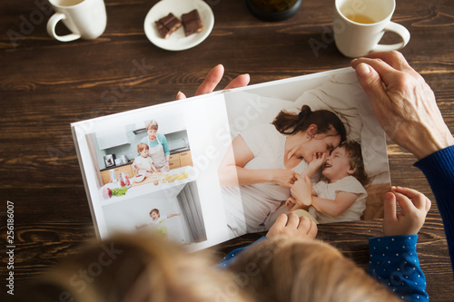 Hand senior woman and child holding a family photo album against the background of the a wooden table. photo